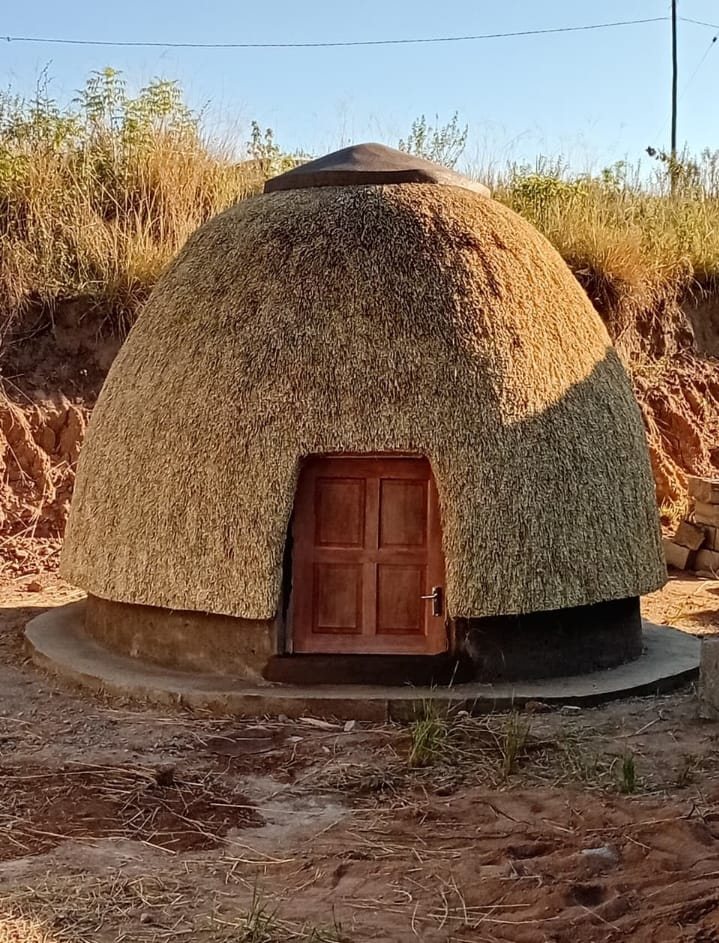 A dome-shaped thatch structure finished on a concrete slab with a timber door.