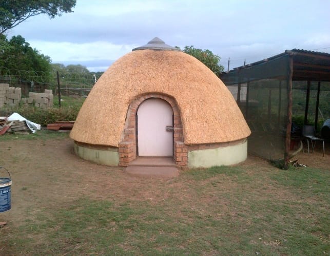 A traditional thatched dome rondavel on a brick base, fully completed.